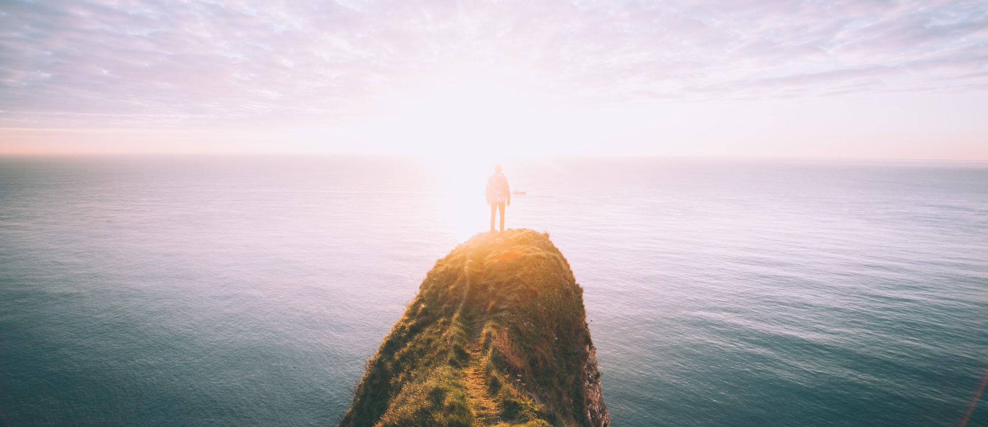 A Person Standing on a Cliff Overlooking a Vast Ocean